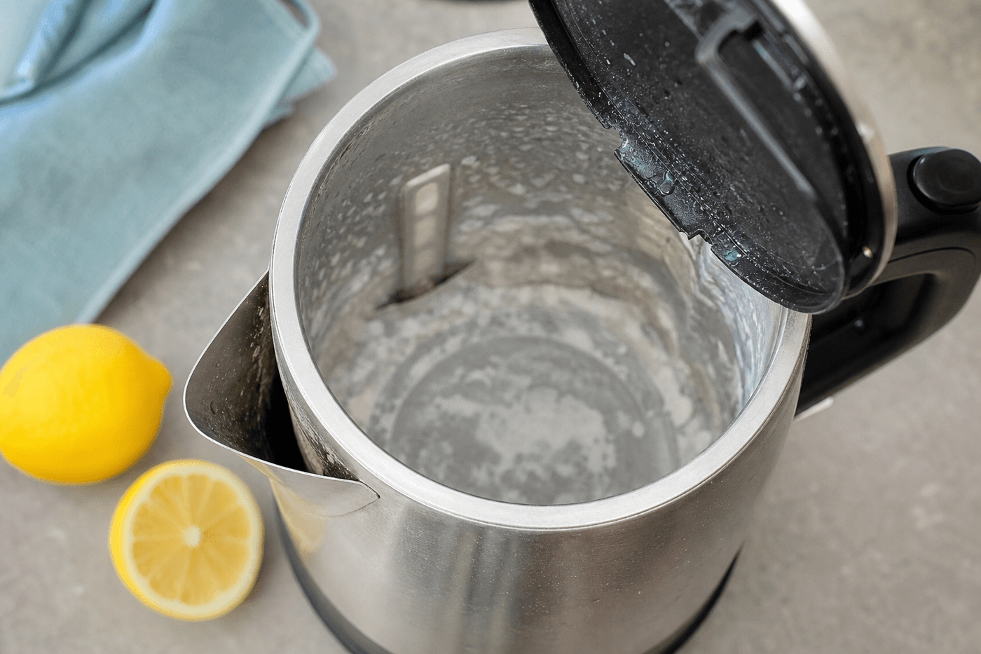 Intérieur d'une bouilloire électrique en inox couvert de dépôts de calcaire blancs, citron coupé à côté