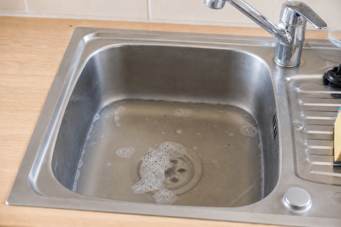Évier de cuisine en inox rempli d'eau savonneuse qui s'écoule mal par la bonde