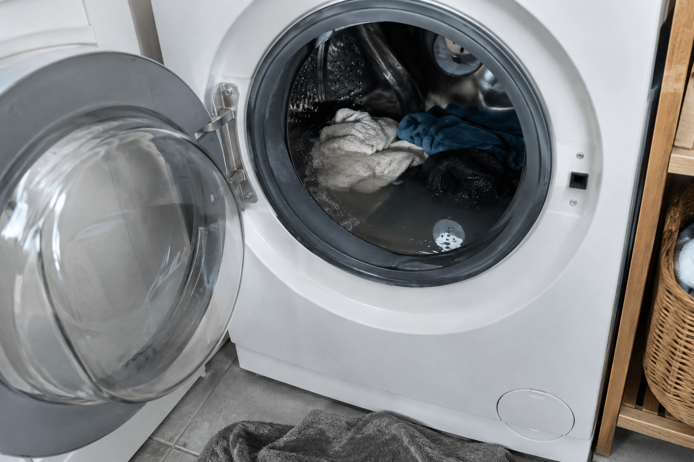 Lave-linge au hublot ouvert avec de l'eau stagnante et du linge dans le tambour