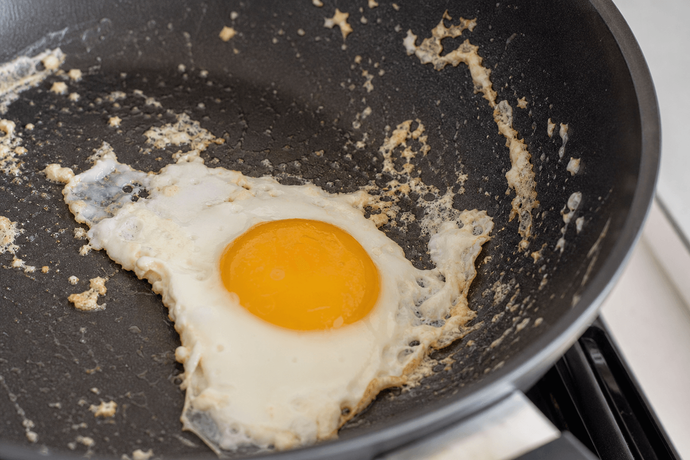 Œuf au plat qui colle et accroche au fond d'une poêle antiadhésive, gros plan sur la cuisson en cours