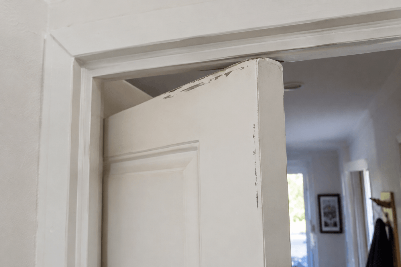 Haut d'une porte intérieure blanche qui frotte contre son encadrement, peinture usée sur le chant